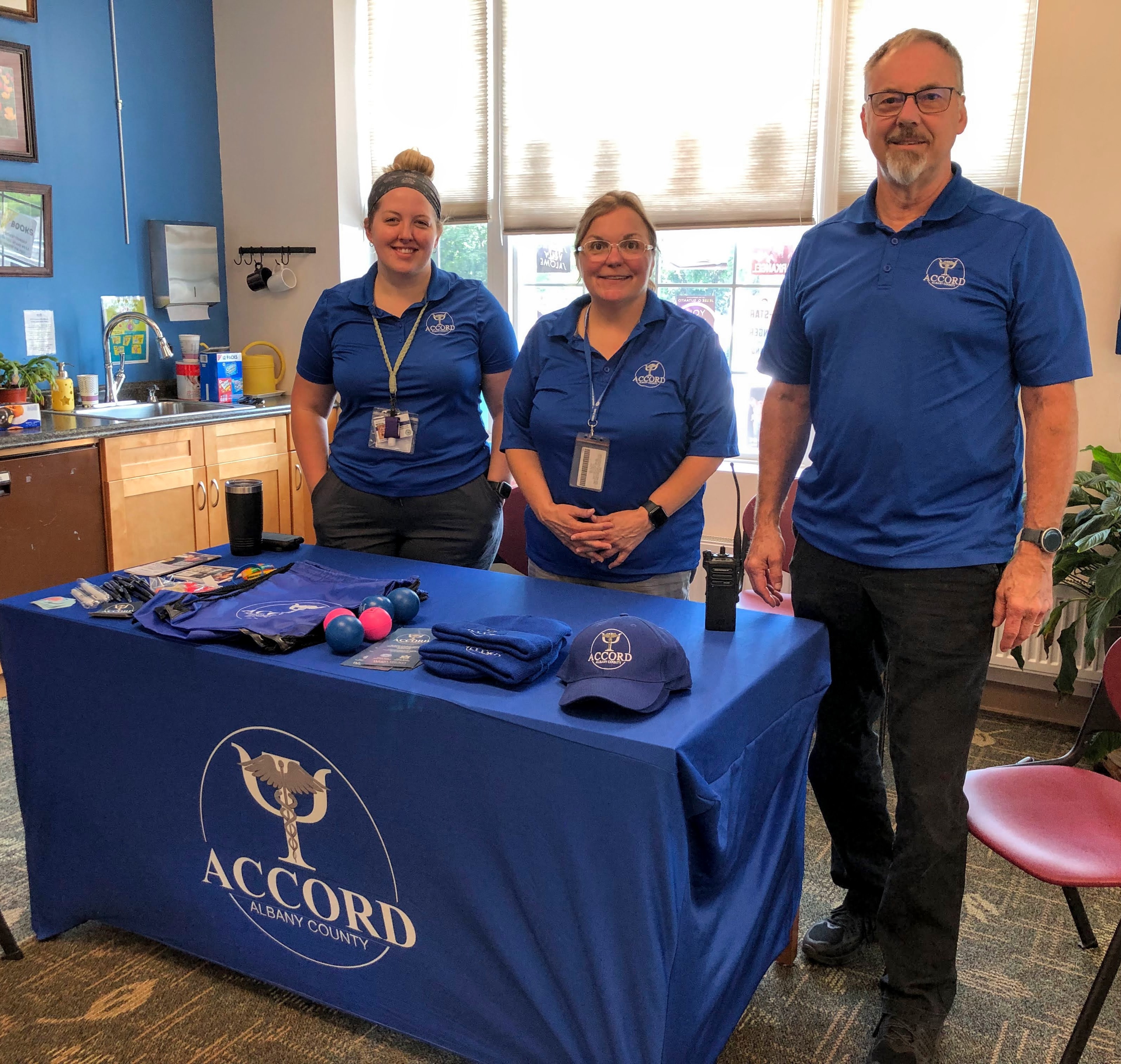 3 staff members from Accord stand behind a table with a blue tablecloth and Accord materials 