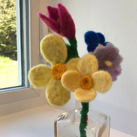 small yellow, purple, blue and pink flowers made out of felt and displayed in a small glass vase
