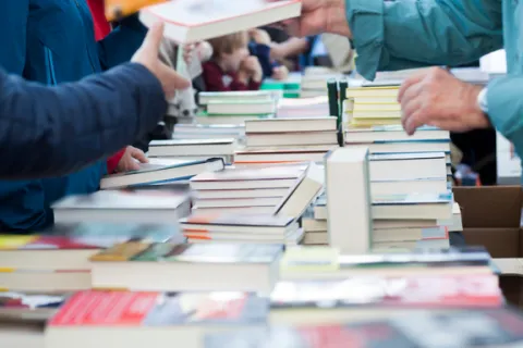 Books in several piles on a table. Two people are exchanging a book in the foreground.