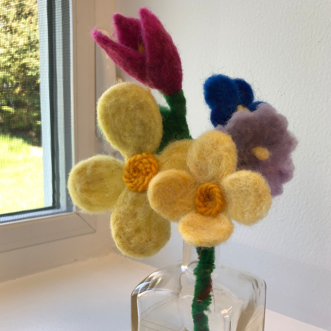 small yellow, purple, blue and pink flowers made out of felt and displayed in a small glass vase